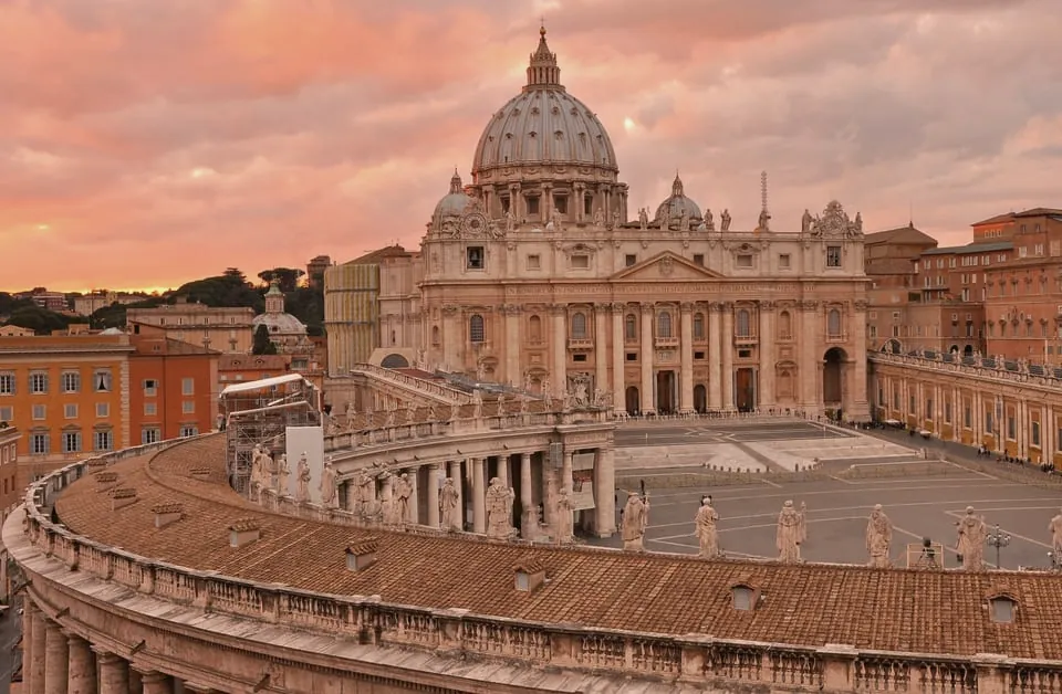 A Basílica de São Pedro e a colunata de Bernini sob o céu alaranjado do fim de tarde.